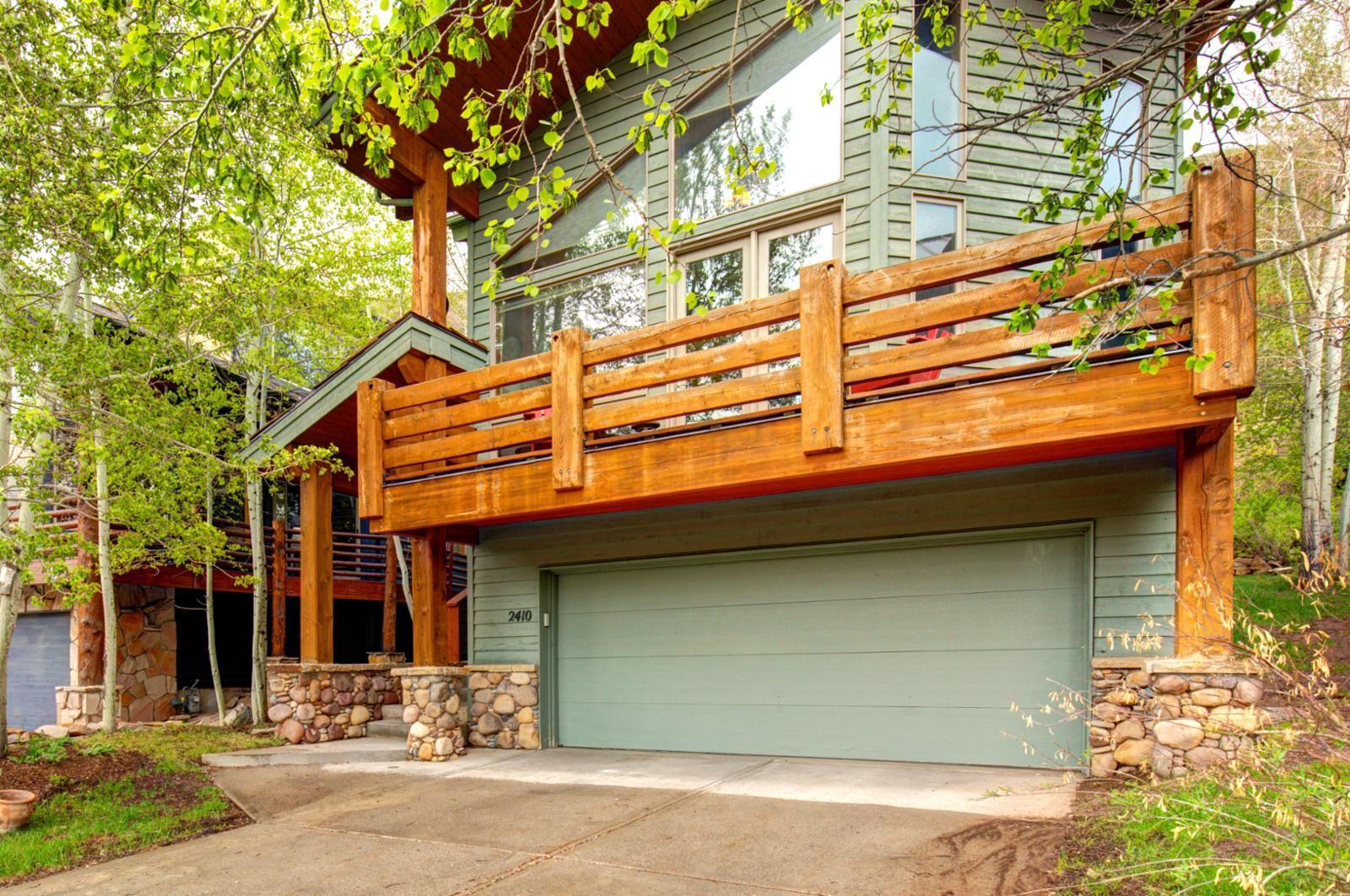 A two-story house with a stone foundation, a green garage door, and a wooden deck.