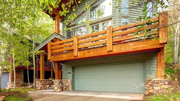 A two-story house with a stone foundation, a green garage door, and a wooden deck.