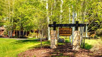 A wooden sign with "Nordic Village" written on it, supported by stone pillars, with trees and a building in the background.