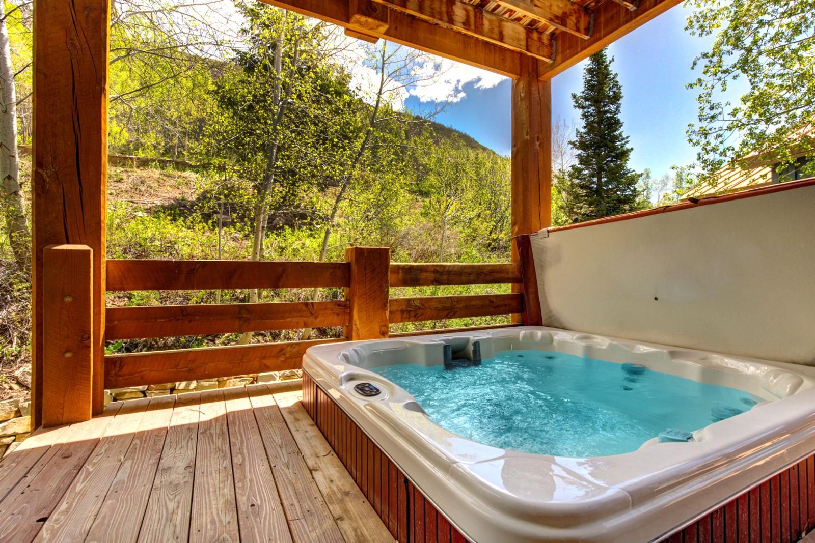 Eine Holzterrasse mit Whirlpool, umgeben von einem Holzzaun und Bäumen.