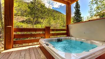A wooden deck with a hot tub, surrounded by a wooden fence and trees.