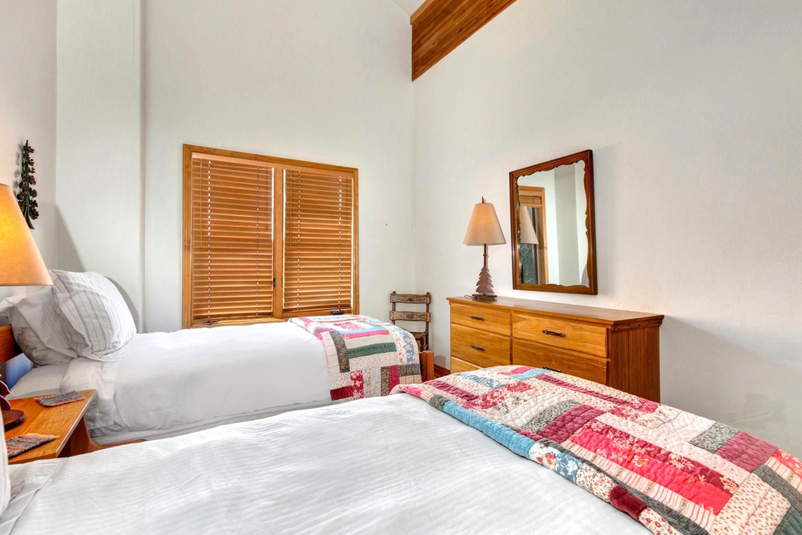 A bedroom with two beds, wooden blinds, a dresser, and a mirror.