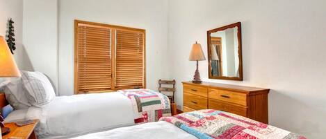 Quarto com duas camas, venezianas de madeira, cômoda e espelho.