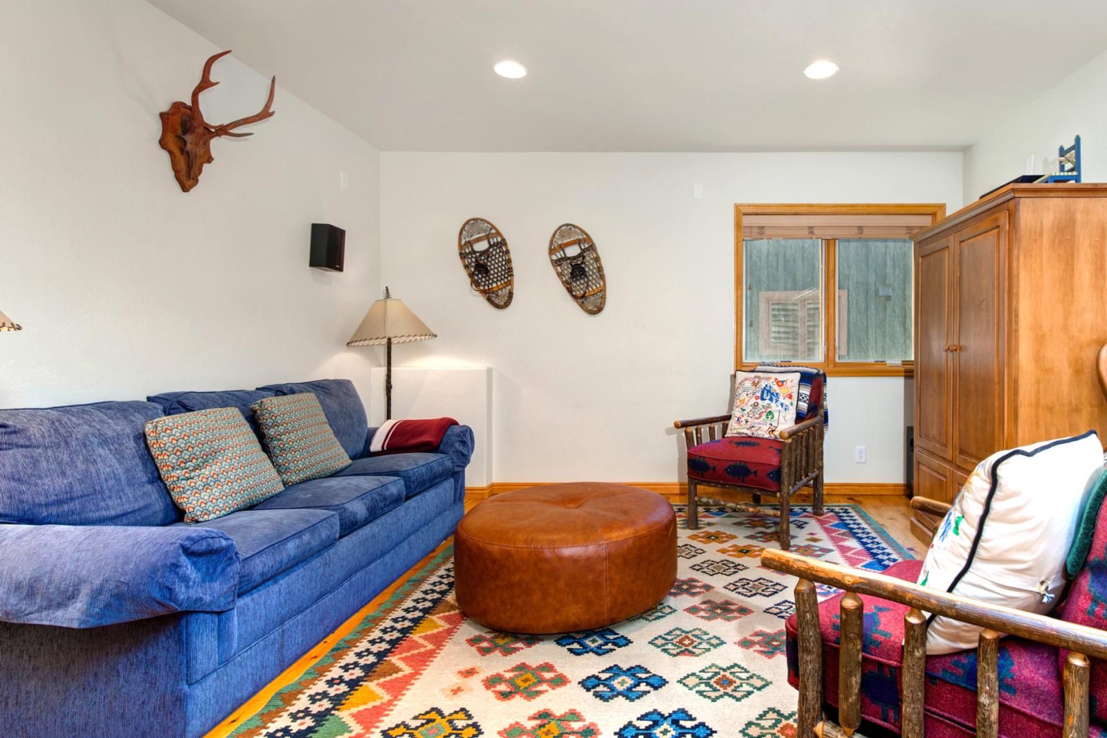 A living room with a blue sofa, a wooden cabinet, a patterned rug, and wall decorations including a skull and two masks.