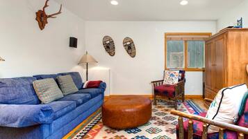 A living room with a blue sofa, a wooden cabinet, a patterned rug, and wall decorations including a skull and two masks.