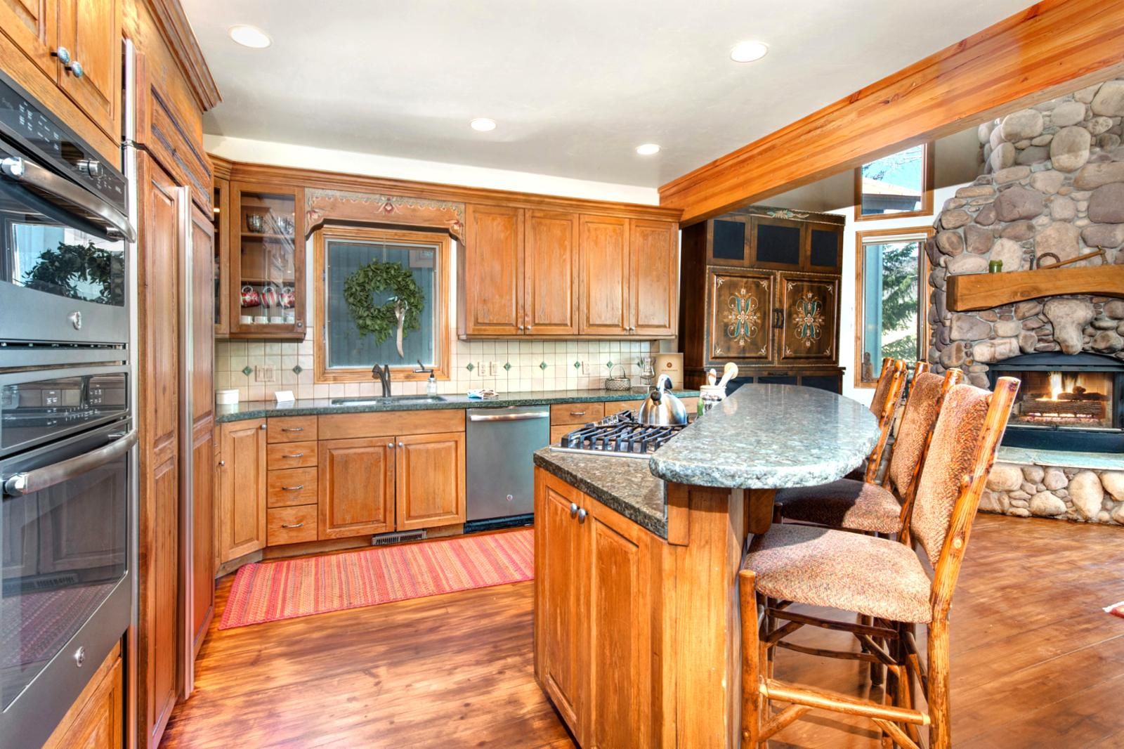 A spacious kitchen with wooden cabinets, a granite countertop, and a stone fireplace.