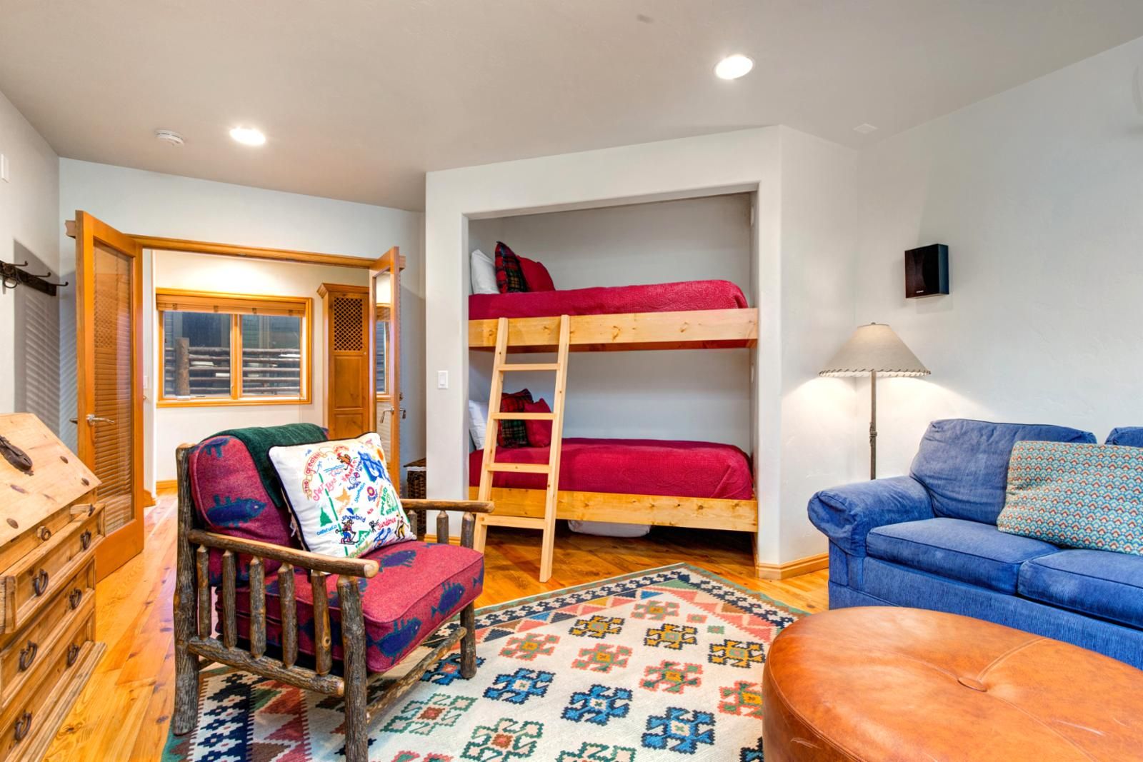A cozy room with bunk beds, a rocking chair, a blue sofa, and a wooden chest of drawers.
