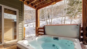 Een hottub op een houten terras met uitzicht op een besneeuwd landschap.