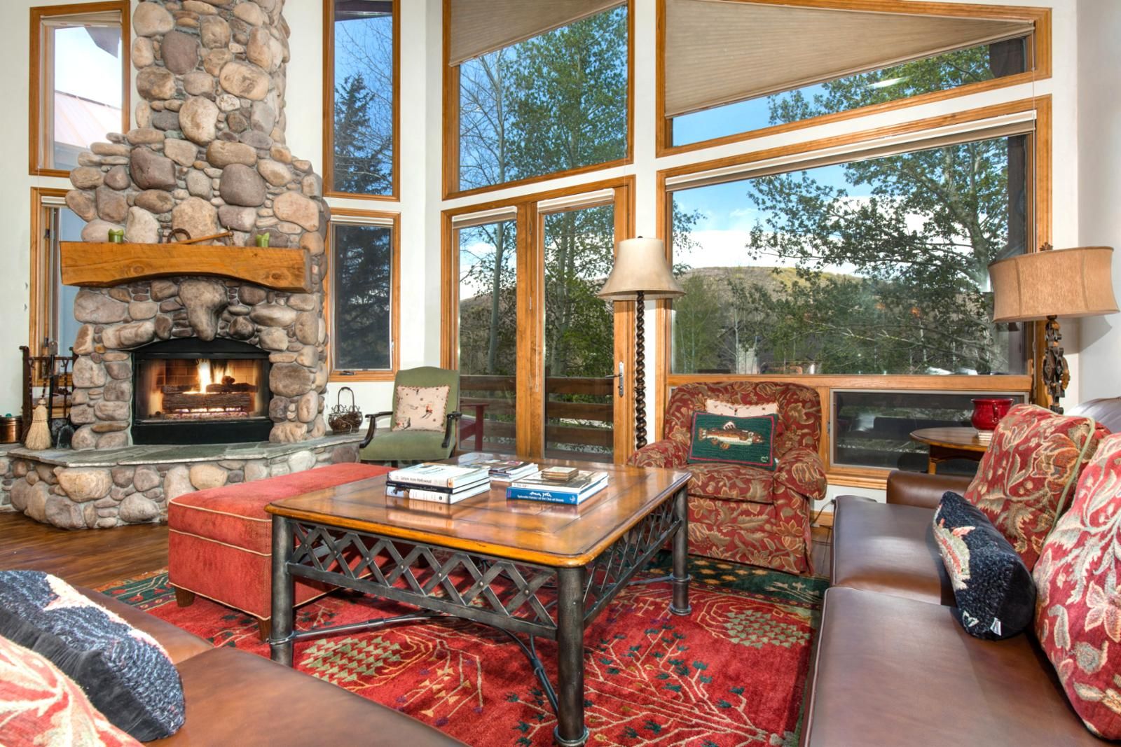 A cozy living room with a stone fireplace, large windows, and comfortable seating.