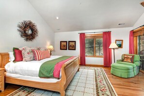 Un dormitorio con una cama de madera, una silla verde, una ventana con cortinas rojas y una lámpara de pie.