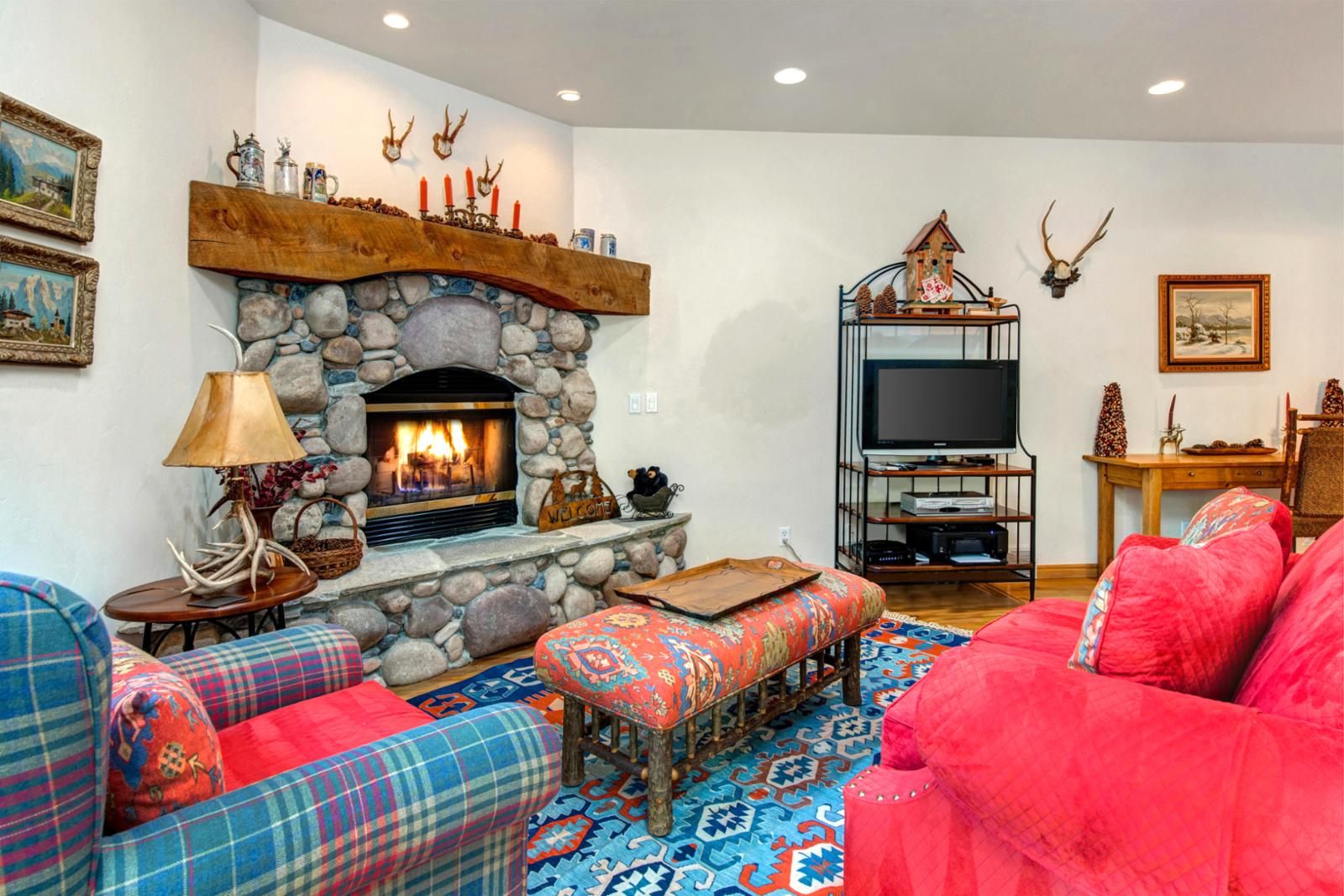 A cozy living room with a stone fireplace, plaid sofas, a television on a wooden stand, and antler decorations.