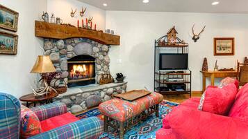 A cozy living room with a stone fireplace, plaid sofas, a television on a wooden stand, and antler decorations.