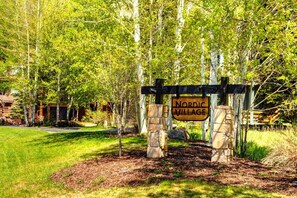 A wooden sign with "Nordic Village" written on it, supported by stone pillars, set in a landscaped area with trees and grass.