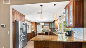 A modern kitchen with wooden cabinets, stainless steel appliances, and a large island with bar stools. - Tropical Resort Style Retreat w/ Pool House 4BR, 3 Bath (Stuart)