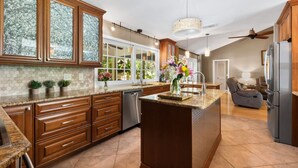 A spacious kitchen with wooden cabinets, a large island, and a view of the outdoors. - Tropical Resort Style Retreat w/ Pool House 4BR, 3 Bath (Stuart)