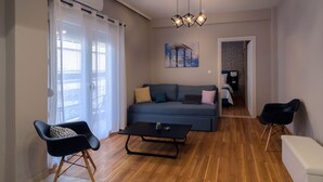 A modern living room with a sofa, a coffee table, and a chair. There is a painting on the wall and a ceiling light fixture. - Athens Chic House Apt B2 42sq.m 1st Floor (Athina)