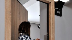 A person entering a room with a wooden door frame, a bed, and a control panel on the wall. - Athens Chic House Apt B2 42sq.m 1st Floor (Athina)