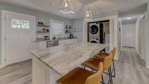 A modern kitchen with a marble island, bar stools, pendant lights, and a built-in washer and dryer. - Fort Jackson Family Abode 3BD 2BA Home RENOVATED (Columbia)