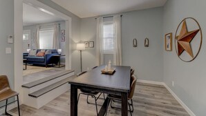 A dining area with a dark wooden table, six chairs, and a small side table with two bottles. There is a staircase leading to another room with a blue sofa and a lamp. - Fort Jackson Family Abode 3BD 2BA Home RENOVATED (Columbia)