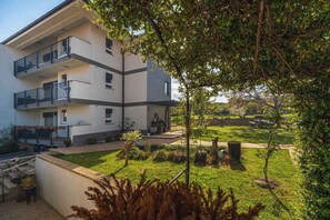 Un immeuble à plusieurs étages doté de balcons, un jardin avec différentes espèces de plantes et un ciel dégagé.