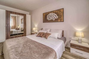 Une chambre à coucher avec un grand lit, un miroir, une table de chevet, une lampe et une œuvre d’art accrochée au mur.