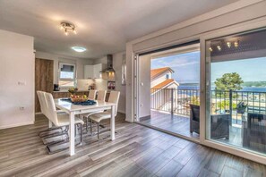 Une cuisine moderne avec des meubles blancs, un coin repas avec une table et des chaises blanches, et un balcon avec vue sur la mer.