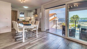 A modern kitchen with a dining area, large sliding glass doors to a balcony, and a view of the sea.