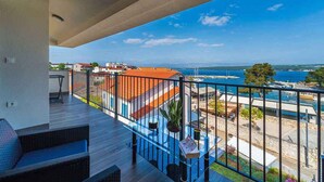 A balcony with a view of the sea, a wooden deck, and outdoor seating.