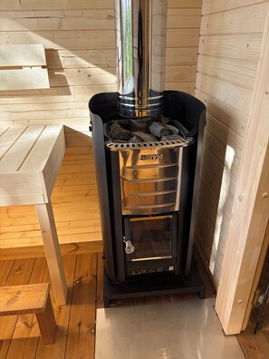 A wood-burning stove with a glass door, a metal grate, and a chimney. - Great house with Spa and Sauna (Bjärnum)