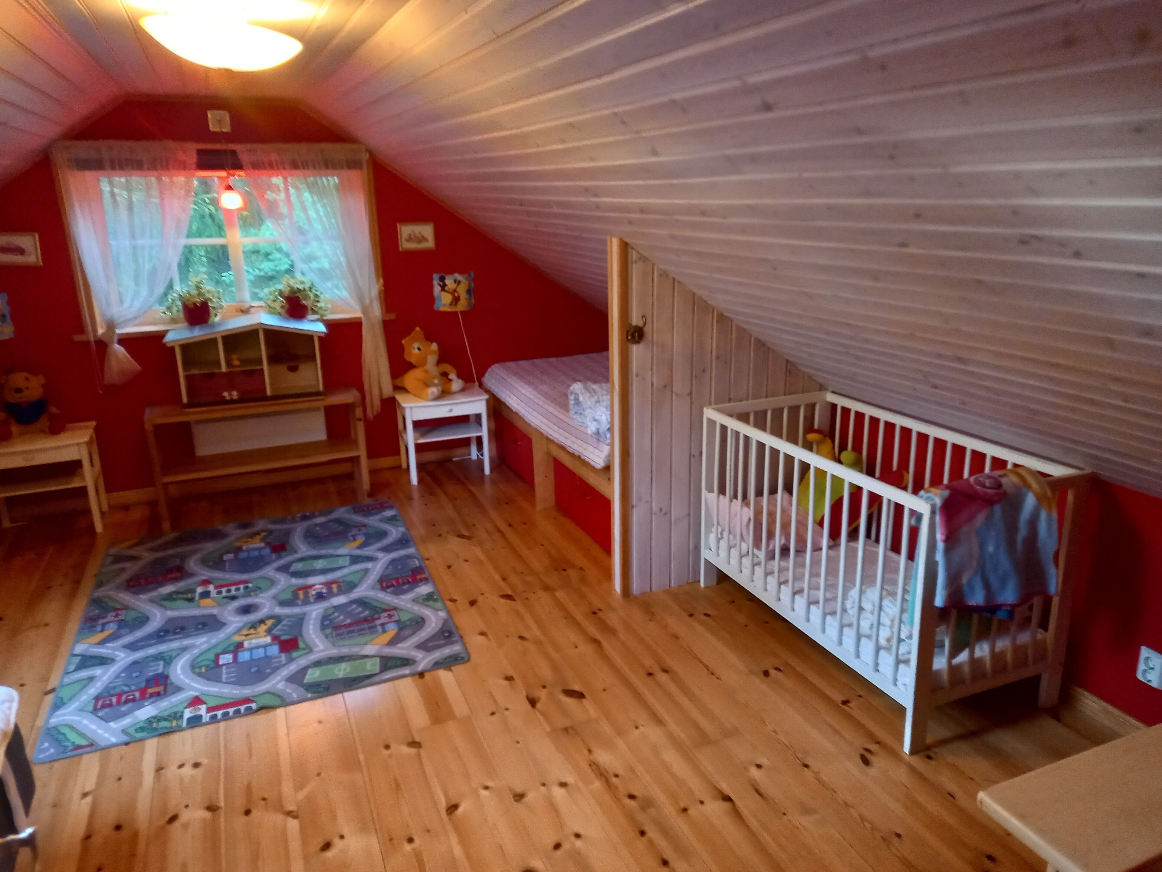 A child's room with a crib, a small table, a chair, a window with curtains, and a rug with a cityscape design.