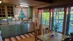 Tunnelmallinen keittiö, jossa on puiset kaapit, ruokapöytä tuoleineen ja suuret ikkunat, joissa on verhot.
