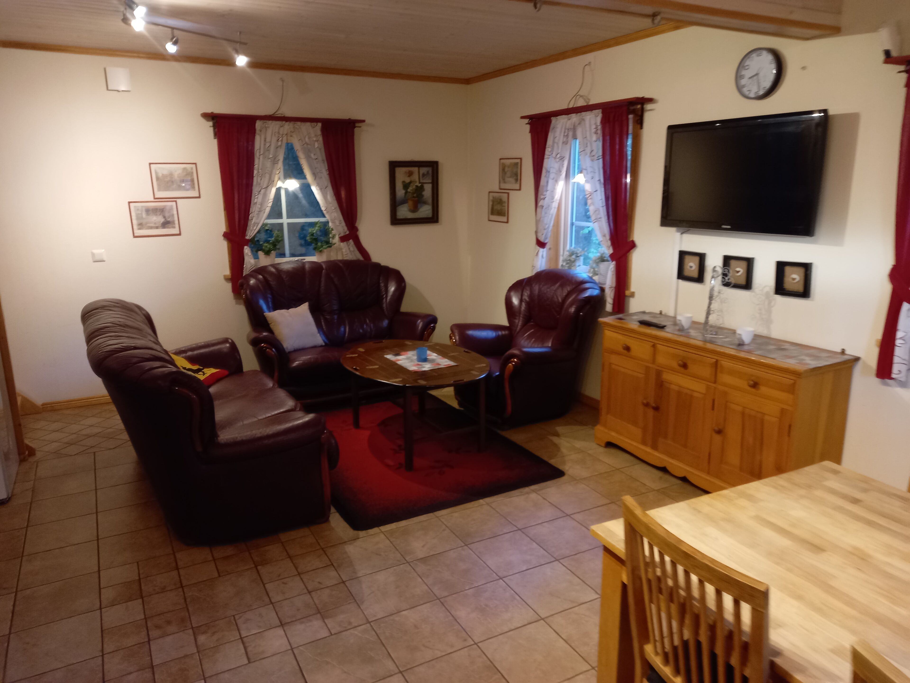 Un salon comprenant un canapé, deux fauteuils, une table basse, un meuble en bois et un téléviseur fixé au mur.