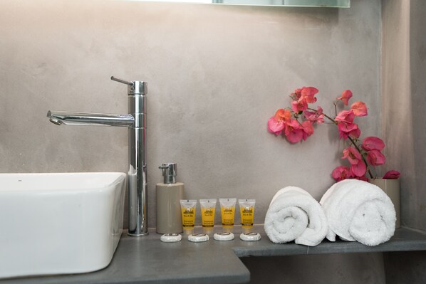 A bathroom with a white sink, a chrome faucet, and a shelf with toiletries and towels.