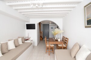 Una sala de estar moderna con sofá, mesa de comedor y sillas. Hay un televisor montado en la pared y un cuadro enmarcado sobre la mesa.