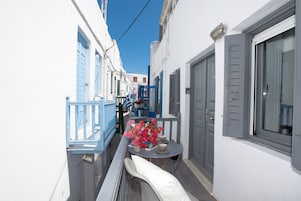 Una calle estrecha con edificios blancos, contraventanas azules y una mesa con un jarrón de flores.