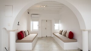 A hallway with a white arched ceiling, a white door at the end, and two seating areas with cushions. - Alessios Mykonian Downtown Houses (Mykonos)