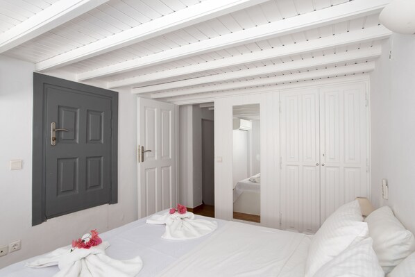 A hotel room with a bed, a grey door, and white walls. - Alessios Mykonian Downtown Houses (Mykonos)