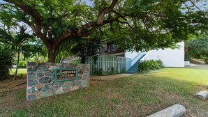 A stone sign with 'Sapphire House Condominiums' written on it, a tree, and a building with a staircase.