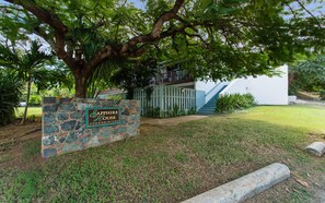 A stone sign with 'Sapphire House Condominiums' written on it, a tree, and a building with a staircase.