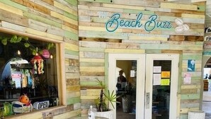 An outdoor seating area with a wooden facade, a sign reading "The Beach Buzz," and a chalkboard menu outside.