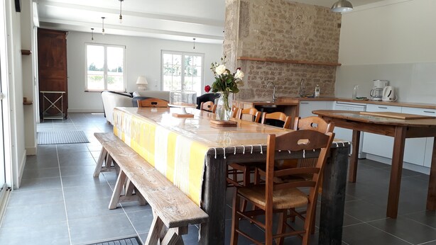 A spacious dining area with a long wooden table, benches, and chairs. There is a kitchen area with a stone wall and modern appliances. - Magnificent gîte with private pool - 12 people - Gîtes Les Grandes Chaumes (Surgères)