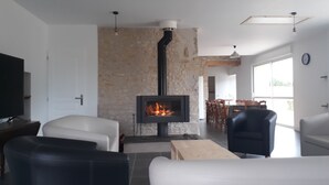 A modern living room with a stone wall, a fireplace, and a dining area with chairs and a table. - Magnificent gîte with private pool - 12 people - Gîtes Les Grandes Chaumes (Surgères)