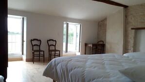 A bedroom with a large bed, two wooden chairs, a small table, and a window. - Magnificent gîte with private pool - 12 people - Gîtes Les Grandes Chaumes (Surgères)