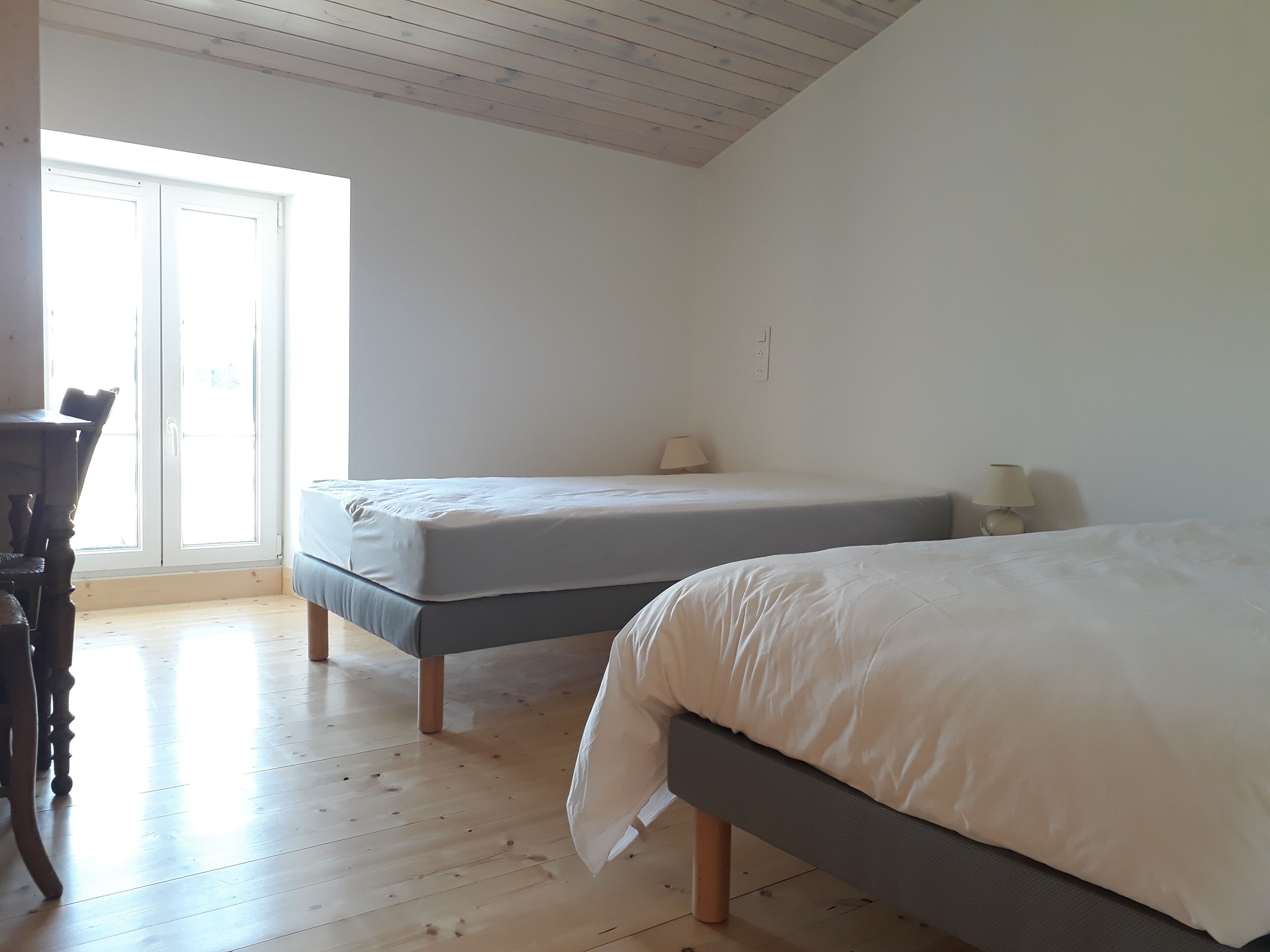 Ein Schlafzimmer mit zwei Betten, Holzboden und einem großen Fenster.