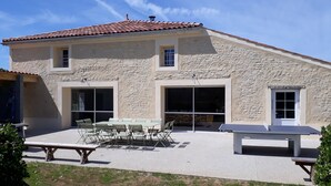 A two-story stone building with a tiled roof, large sliding glass doors, and a patio area with a table and chairs. - Magnificent gîte with private pool - 12 people - Gîtes Les Grandes Chaumes (Surgères)