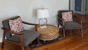 A living room with two grey armchairs, a round wooden coffee table, a floor lamp, and a framed floral artwork on the wall.