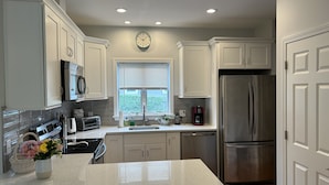 A modern kitchen with white cabinets, stainless steel appliances, a granite countertop, and a window with blinds.