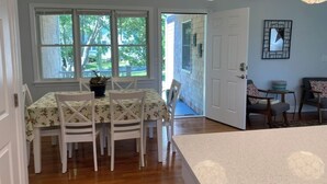 A dining area with a table and chairs, a potted plant, and a view through a door to the outside.