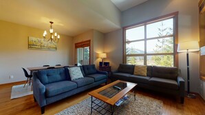 A living room with a blue sofa, a dark grey sofa, a wooden coffee table, and a large window with a view of trees and mountains. - 3 Bedroom plus Den / 2.5 Bath Mountain Star Townhome, Private Hot Tub, Quiet Slope Side location (Whistler)