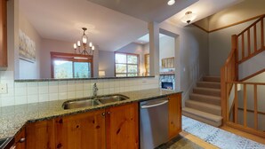 A kitchen with granite countertops, wooden cabinets, a dishwasher, a stone fireplace, and a staircase with wooden railings. - 3 Bedroom plus Den / 2.5 Bath Mountain Star Townhome, Private Hot Tub, Quiet Slope Side location (Whistler)